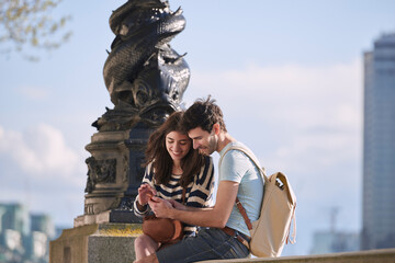 Couple, phone and travel holiday while at statue doing search on internet for map information on tourist trip. Man and woman with cellphone for social media content on foreign city journey in London