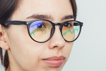 The reflection of the trader's market charts in the glasses of a girl looking at a computer monitor