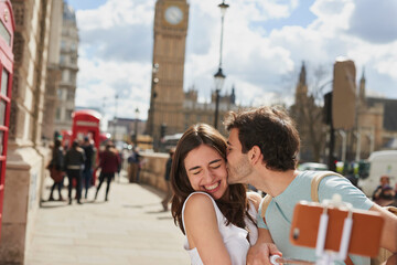 Couple, travel and selfie with kiss outdoor in London for romantic holiday, adventure and love in...