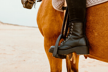 The girl's foot in the stirrup during a horseback ride on Supertubos beach at the end of the day,...