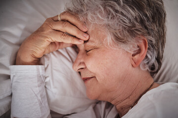 Fototapeta premium Sleep, headache and senior woman in a bed with stress, anxiety and tired. Sick, sad and face of an elderly lady dreaming with depression and sleeping in her bedroom for rest during retirement