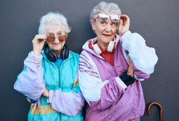 Fashion, funky and friends with a senior woman pair standing outdoor on a gray wall background...