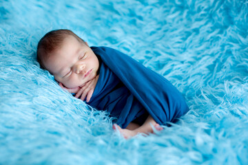 Cute baby boy, peacefully sleeping wrapped in blue wrap