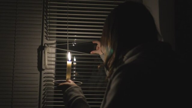 Blackout. A girl in a dark room near the window holds a burning candle in her hands