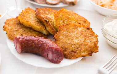 Potato pancakes with fried sausage on white plate