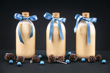 Homemade eggnog in bottles with pine cones and blue balls on dark background