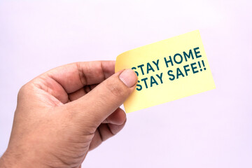 Male hand holding yellow paper with stay home, stay safe written on it. Quarantine concept. Corona virus concept