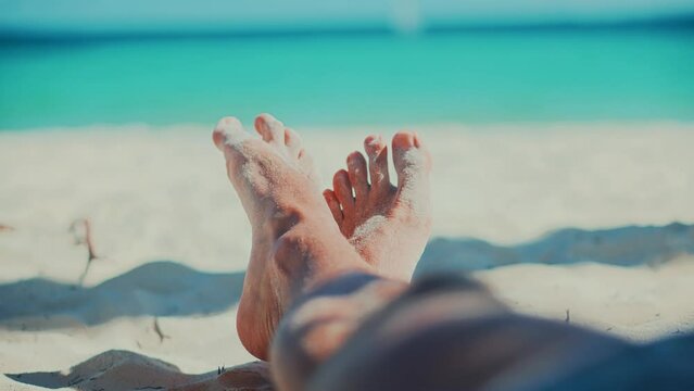 Resting on white sand, toes wiggle and move in warm sunshine.