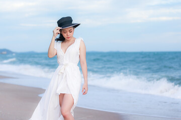 Fototapeta na wymiar Young asian woman wearing white dress and black hat walking relax on the beach, enjoying the sea and Happy summer vacation