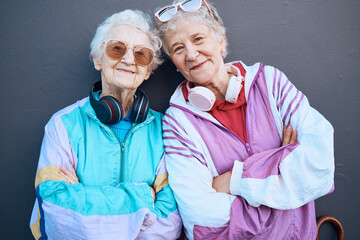 Portrait, fashion and friends with a senior woman pair standing arms crossed outdoor on a gray wall...