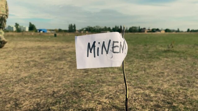 A man in a military uniform walks through a mined area against the background of Minen inscription. Demining of the territory by sappers.