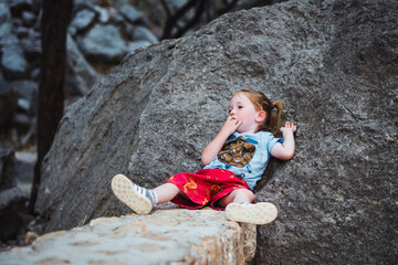 Small child resting and relaxing while lying on a rock sucking on his fingers, taking a break while hiking in a natural park. Overcoming difficulty and self soothing.