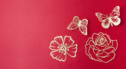 A carve of white paper butterfly and flower on a red cardboard background.