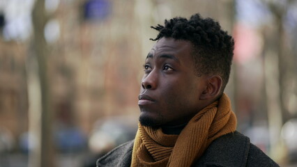 Pensive thoughtful black African man standing outside thinking and observing city