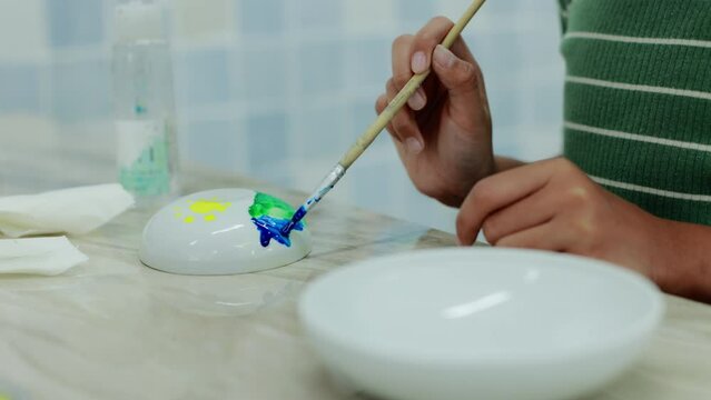 Child using paintbrush is painting on ceramic bowl with oil color