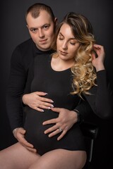 pregnant woman in a black bodysuit and a man on a black background. Long curly hair, beautiful couple, husband and wife, future parents. stylish pregnancy. portrait