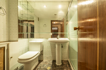 Small bathroom with pedestal porcelain sink, large mirror on the wall and old tiles