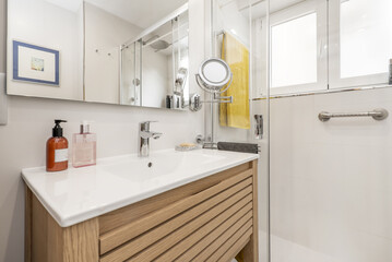 Small bathroom with porcelain sink on oak cabinet, sliding shower stall, frameless mirror and round...