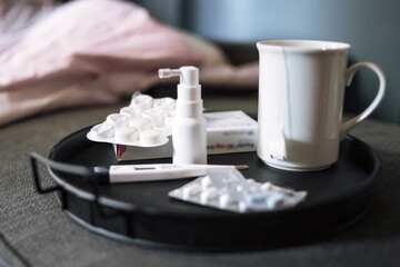 Medicines for seasonal colds. Nasal spray, thermometer and pills on a tray in the bed.