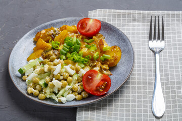Baked potatoes with cheese and mushrooms garnished with tomatoes sprinkled with green onions in a plate on a gray napkin next to a fork on a gray background.
