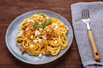 Homemade bolognese pasta on a plate next to a checkered napkin and a fork.