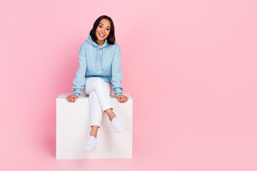 Full length photo of pretty adorable girl dressed blue sweatshirt having rest white cube chair empty space isolated pink color background