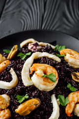 delicious black rice with shrimps and seafood on a black wooden rustic background