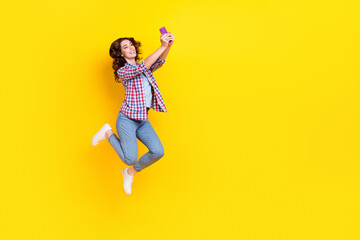 Fototapeta na wymiar Full size photo of gorgeous cheerful woman curly hair checkered shirt flying making selfie on phone isolated on yellow color background