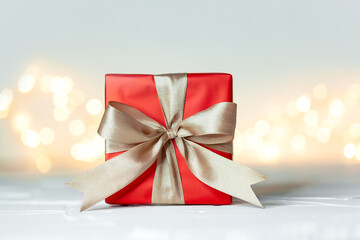 Gift xmas box wrapped with red paper and bow on festive boke background. Christmas or birthday...