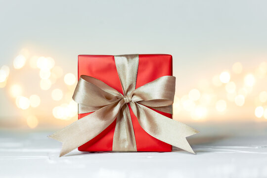 Gift xmas box wrapped with red paper and bow on festive boke background. Christmas or birthday concept.