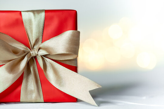 Gift xmas box wrapped with red paper and bow on festive boke background. Christmas or birthday concept.