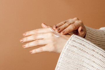 Woman applying cream on hands at brown background. Hands with moisturizing cream, skin care, aesthetic concept, copy space
