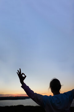closeup of the silhouette of a woman performing a yoga asana at sunrise looking at the sea. vertical image with big copy space