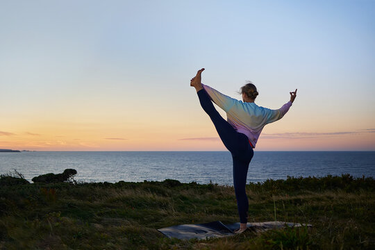horizontal image of a woman performing yoga poses in front of the sea