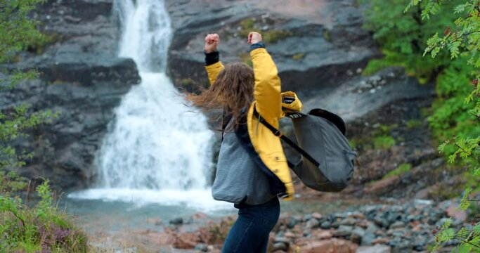 Hiking, travel and woman dance by waterfall in nature on vacation or trip. Carefree, freedom and happy female hiker having fun, dancing in rain and enjoying quality time alone on adventure by river.