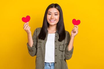 Photo of young smiling vietnamese girl wear khaki trendy shirt brunette hair hold red love symbols valentine day isolated on yellow color background
