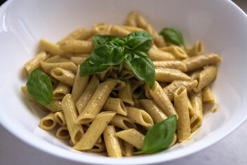 Penne pasta with spinach pesto sauce and basil leaves. High angle view. Selective Focus Basil.