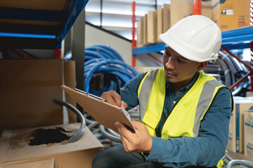 Asian man wearing reflective jacket holding checklist paper standing in factory warehouse.