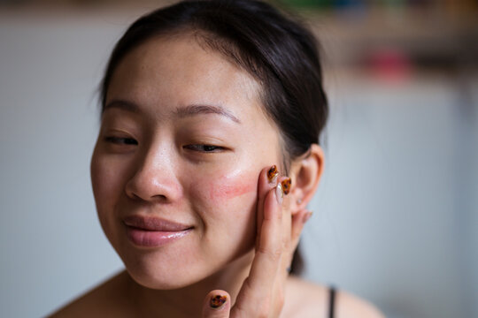 Asian woman applying rouge on cheek