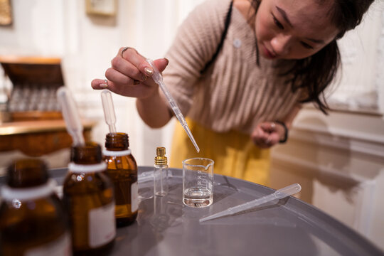 Female master dripping essential oil into glass bottle at home - Powered by Adobe