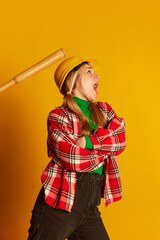 Retro style portrait of young happy blond girl in vintage style clothes with baseball bat isolated on yellow background. Vivid emotions, happiness, hobbies and fashion