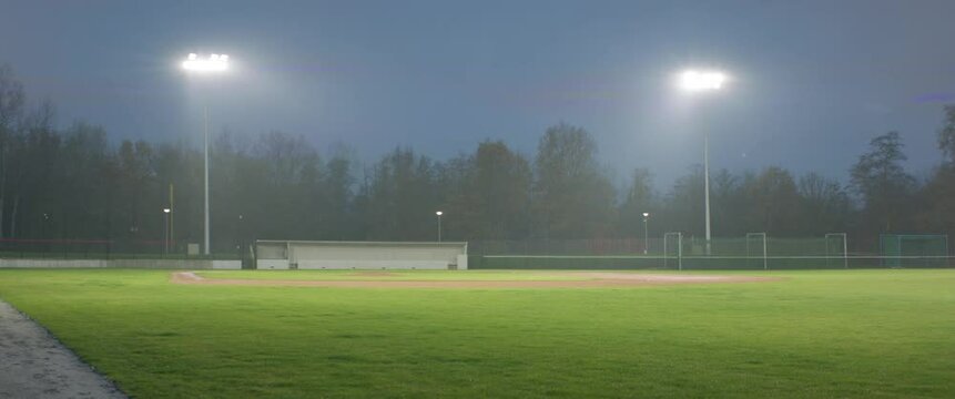WIDE view of empty baseball field at dusk under heavy rain. Stadium flood lights are turning on and off. Shot with 2x anamorphic lens