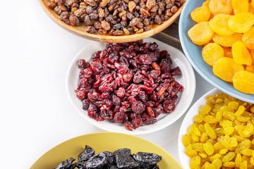 Dried apricots, cranberries, raisins, and prunes on a plates on a white background. Dry fruits assortment. Healthy sweet snack - mix of organic dry fruits. Vegan and vegetarian products