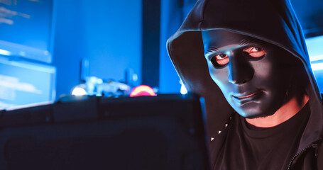 A hacker wearing a mask to cover his face is using computer to hack data to get ransom from victims.