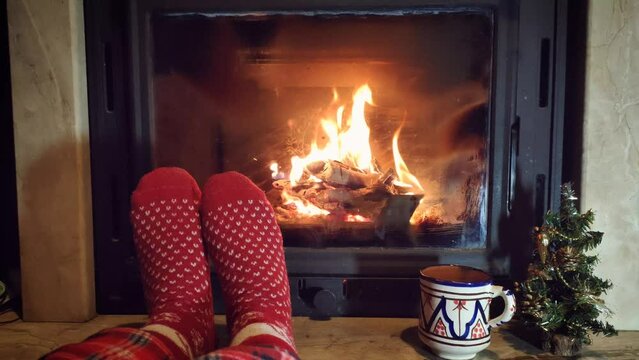 Feet in warm red socks on the background of the fireplace in winter. Bright burning firewood in  fireplace. Christmas holidays concept.