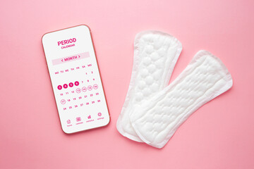 Menstruation calendar application on a smartphone lies isolated on a pink background with two women pads