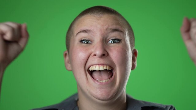 Closeup slow motion portrait of amazed non binary gender fluid woman 20s shocked, saying YES. Attractive female surprised isolated on solid green screen background.