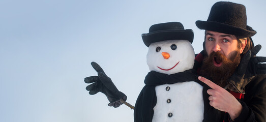Merry christmas and happy new year. Funny winter snow man in hat play with snowman outdoor. Man pointing on snowman on winter outdoor background. Snow man for winter banner.