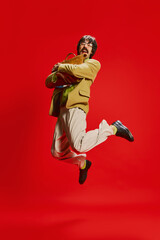 Portrait of stylish man with moustache posing in vintage suit isolated over red background. Jumping with briefcase