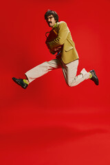 Portrait of stylish man with moustache posing in vintage suit in a jump isolated over red background